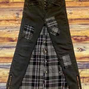 May include: A unique, handmade denim skirt with a plaid shirt panel and patches. The skirt is dark gray with gold zippers on the sides. Plaid patches in gray, black, and purple add detail. The skirt is a creative blend of materials.