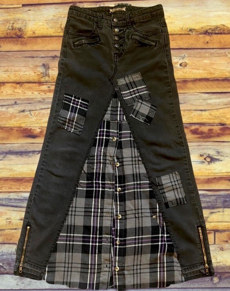 May include: A unique, handmade denim skirt with a plaid shirt panel and patches. The skirt is dark gray with gold zippers on the sides. Plaid patches in gray, black, and purple add detail. The skirt is a creative blend of materials.