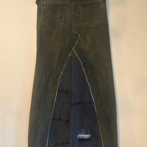 Puede incluir: Falda larga de mezclilla verde oscuro con cintura alta y dise&ntilde;o de espalda dividida. La falda presenta dos bolsillos traseros y un panel de mezclilla azul oscuro contrastante en la abertura, con parches desgastados y bordes deshilachados. La falda cuelga de una percha de madera.