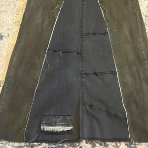 Puede incluir: Una falda larga de mezclilla oscura con un dise&ntilde;o de patchwork &uacute;nico. La falda presenta un panel central de mezclilla gris oscuro, flanqueado por paneles de mezclilla verde oliva. Las costuras blancas y los bordes deshilachados a&ntilde;aden detalles.