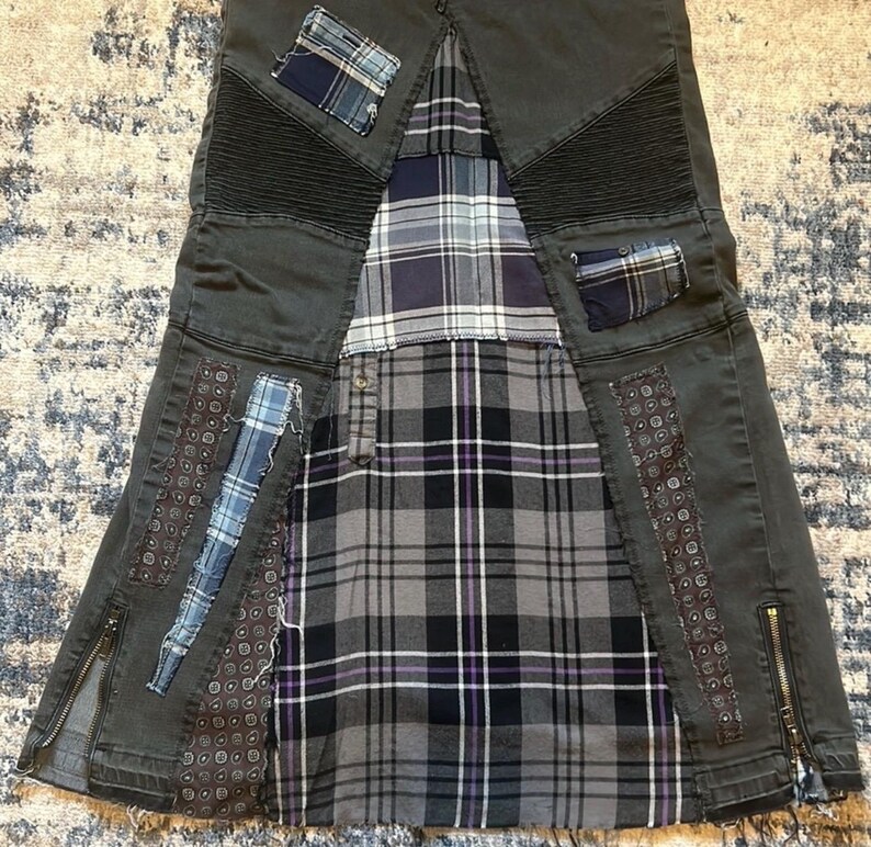 Puede incluir: Falda vaquera gris oscuro con dise&ntilde;o patchwork. La falda presenta un estampado de cuadros en tonos grises, negros y morados. Parches de tela azul y estampada est&aacute;n cosidos a la falda. La falda tiene cremalleras en los laterales y un estilo &uacute;nico y atrevido.