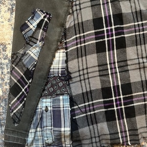 Puede incluir: Primer plano de una prenda de patchwork con una mezcla de telas a cuadros y estampadas en tonos grises, negros, azules y morados. La prenda tiene una base de mezclilla gris oscuro con parches de diferentes telas cosidas, creando un dise&ntilde;o &uacute;nico y texturizado.