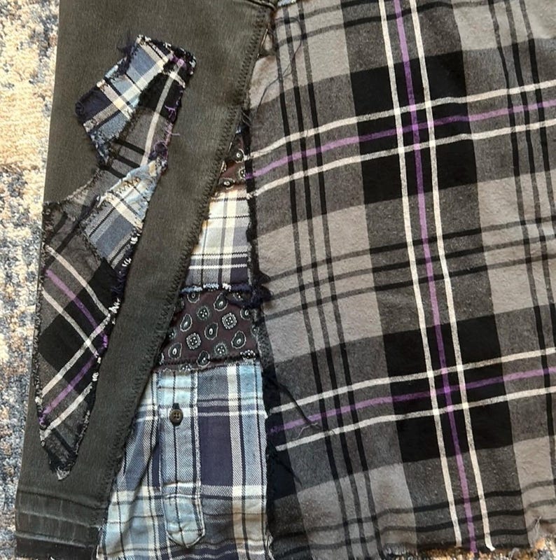 Puede incluir: Primer plano de una prenda de patchwork con una mezcla de telas a cuadros y estampadas en tonos grises, negros, azules y morados. La prenda tiene una base de mezclilla gris oscuro con parches de diferentes telas cosidas, creando un dise&ntilde;o &uacute;nico y texturizado.