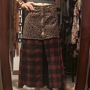 May include: A two-tone skirt with a leopard print top and a red and black plaid bottom. The skirt has a gold zipper down the front and button closures. The skirt is a unique, stylish piece.