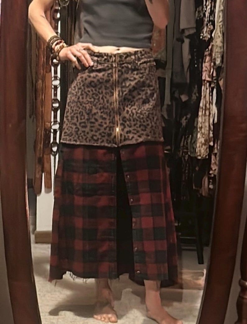 May include: A two-tone skirt with a leopard print top and a red and black plaid bottom. The skirt has a gold zipper down the front and button closures. The skirt is a unique, stylish piece.