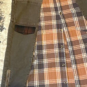 May include: An olive green jacket with a plaid flannel lining. The jacket features a quilted shoulder detail, a small plaid pocket, and a zipper on the lower sleeve. The plaid lining is brown, tan, and navy blue.