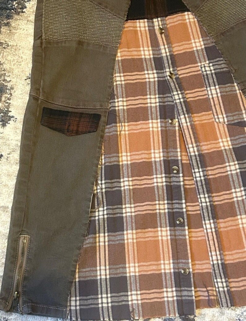 May include: An olive green jacket with a plaid flannel lining. The jacket features a quilted shoulder detail, a small plaid pocket, and a zipper on the lower sleeve. The plaid lining is brown, tan, and navy blue.