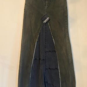 Puede incluir: Una falda larga de mezclilla verde oliva con una abertura frontal, que revela un panel de mezclilla gris m&aacute;s oscuro. La falda presenta un dise&ntilde;o de patchwork y un dobladillo deshilachado, que ofrece una est&eacute;tica &uacute;nica y desgastada. La falda tiene un dise&ntilde;o cl&aacute;sico de cinco bolsillos.