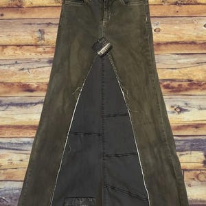 Puede incluir: Falda larga de mezclilla verde oliva con un dise&ntilde;o &uacute;nico. La falda presenta una abertura frontal con un panel gris m&aacute;s oscuro, costuras blancas y un aspecto desgastado. Tiene un dise&ntilde;o cl&aacute;sico de cinco bolsillos.