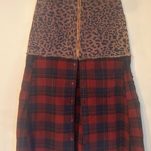 May include: A unique skirt featuring a leopard print denim top with a gold zipper and a red and black plaid flannel bottom. The skirt has a raw hem and button details.