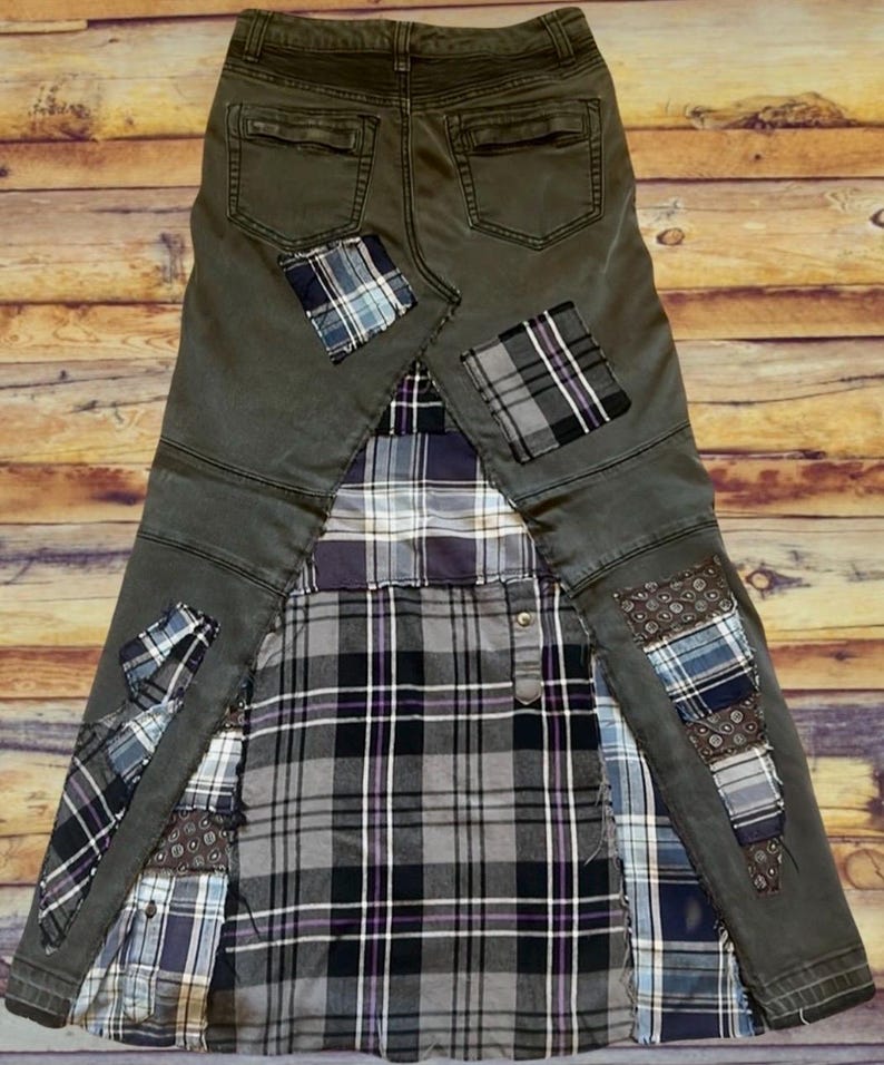 Puede incluir: Una falda &uacute;nica, hecha a mano, construida con mezclilla reciclada y telas a cuadros. La falda presenta una base de mezclilla verde oscuro con detalles de patchwork a cuadros en tonos azules, grises y morados. El dise&ntilde;o incorpora los bolsillos traseros de los jeans.