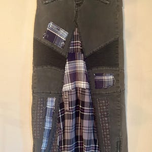 Puede incluir: Falda vaquera gris oscuro con detalles de patchwork. La falda presenta una mezcla de texturas, incluyendo paneles acolchados e inserciones de tela a cuadros en tonos morados, azules y grises. Tiene cierre de bot&oacute;n y cremallera, y costuras decorativas.