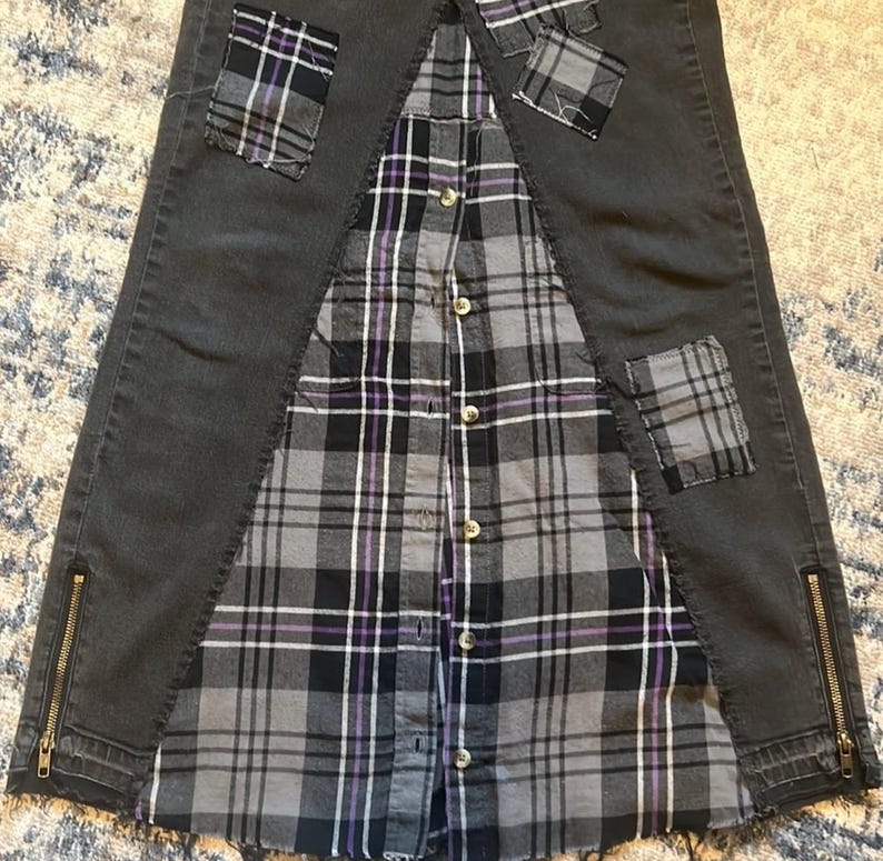 May include: A unique skirt design featuring a combination of dark gray denim and a gray, black, and purple plaid shirt. The denim sections have zipper details and plaid patches. The shirt is buttoned down the front.