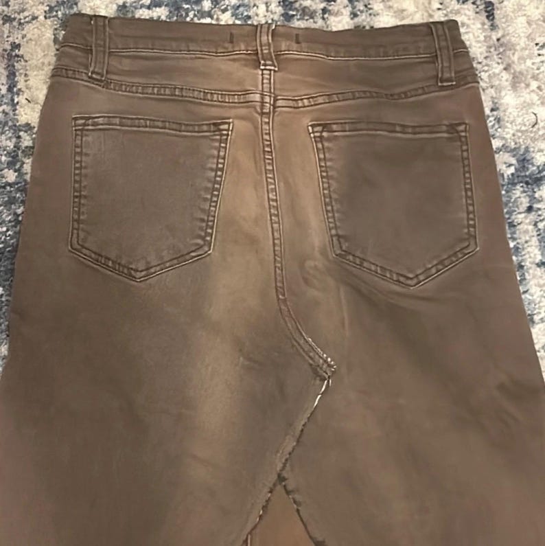 May include: Back view of brown denim pants with two back pockets. The pants have a classic five-pocket design and a straight leg cut. The denim is a solid, neutral brown color.