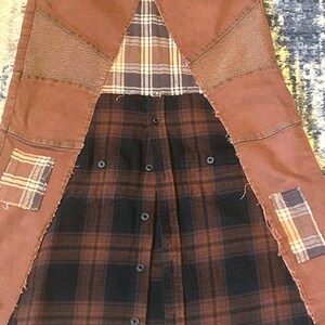 May include: A repurposed garment featuring brown denim pants with patchwork details and a button-down plaid shirt. The design incorporates various plaid patterns and textures, creating a unique, upcycled aesthetic. The garment has a deconstructed, handcrafted appearance.