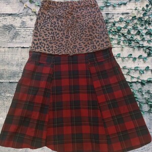 May include: A two-tone skirt featuring a brown leopard print denim top and a red and black plaid bottom. The skirt has a classic design with a pleated front and a casual style.