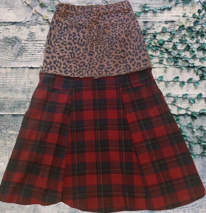 May include: A two-tone skirt featuring a brown leopard print denim top and a red and black plaid bottom. The skirt has a classic design with a pleated front and a casual style.