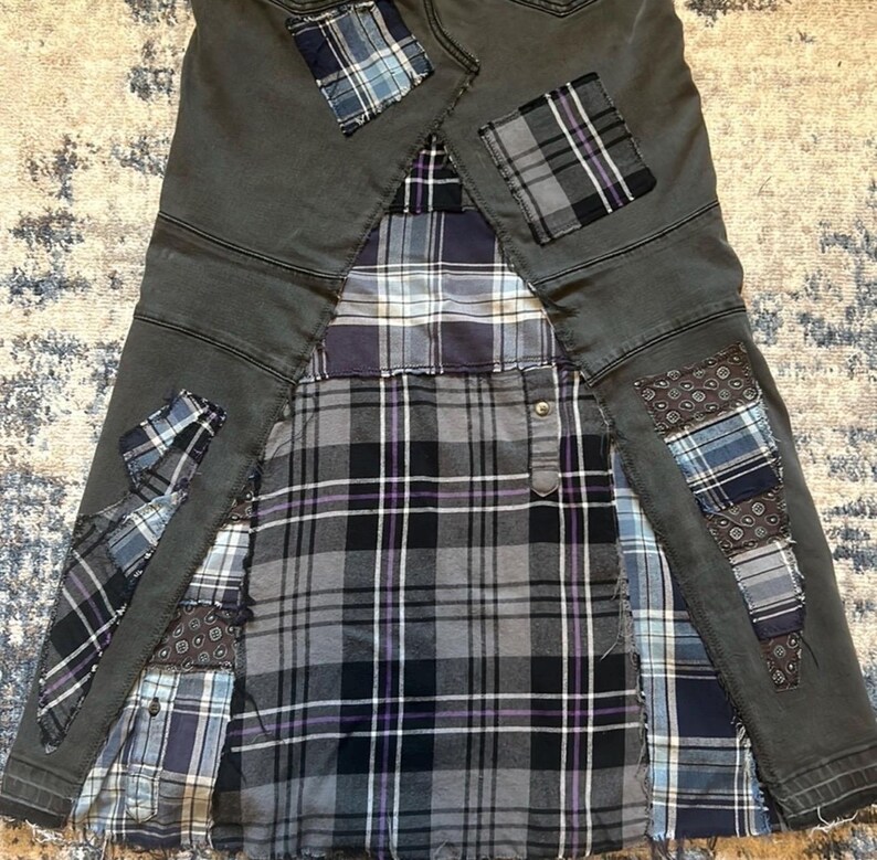 Puede incluir: Falda vaquera gris con detalles de patchwork. La falda presenta un estampado de cuadros en tonos grises, negros y morados. Parches de varias telas de cuadros y estampadas est&aacute;n cosidos en la falda, a&ntilde;adiendo un aspecto &uacute;nico y artesanal.