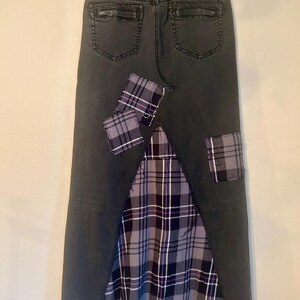 May include: Dark gray denim skirt with a plaid fabric panel and patches. The skirt features a distressed hem and back pockets. The plaid fabric incorporates shades of purple, gray, and white, adding a unique design element to the garment.