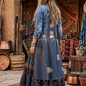 May include: A long-sleeved denim jacket with a distressed finish and patchwork details, worn over a tiered, floor-length skirt featuring dark blue patterned fabric and a lace hem. The outfit includes a brown leather belt with silver-toned buckles.