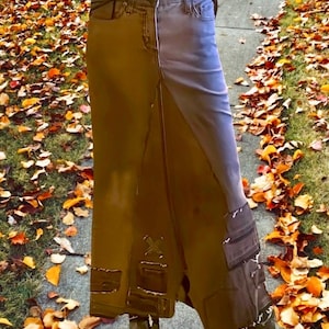 May include: A two-tone denim skirt in shades of brown and blue. The skirt features a high waist, pockets, and decorative patches. The skirt is long, reaching the ankles, and is worn with brown boots.