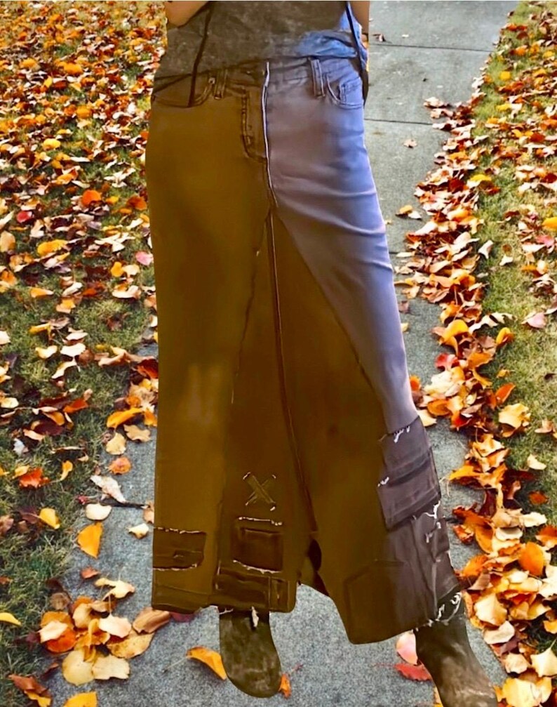 May include: A two-tone denim skirt in shades of brown and blue. The skirt features a high waist, pockets, and decorative patches. The skirt is long, reaching the ankles, and is worn with brown boots.
