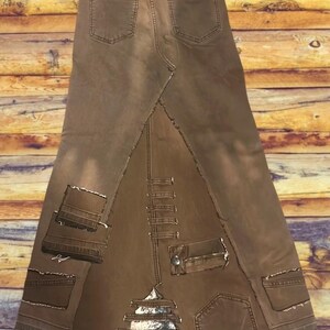 May include: A brown denim skirt with a unique design. The skirt features a patchwork construction with visible seams and pockets. The skirt has a high waist and a flared silhouette, with a distressed look. The skirt is made of denim.
