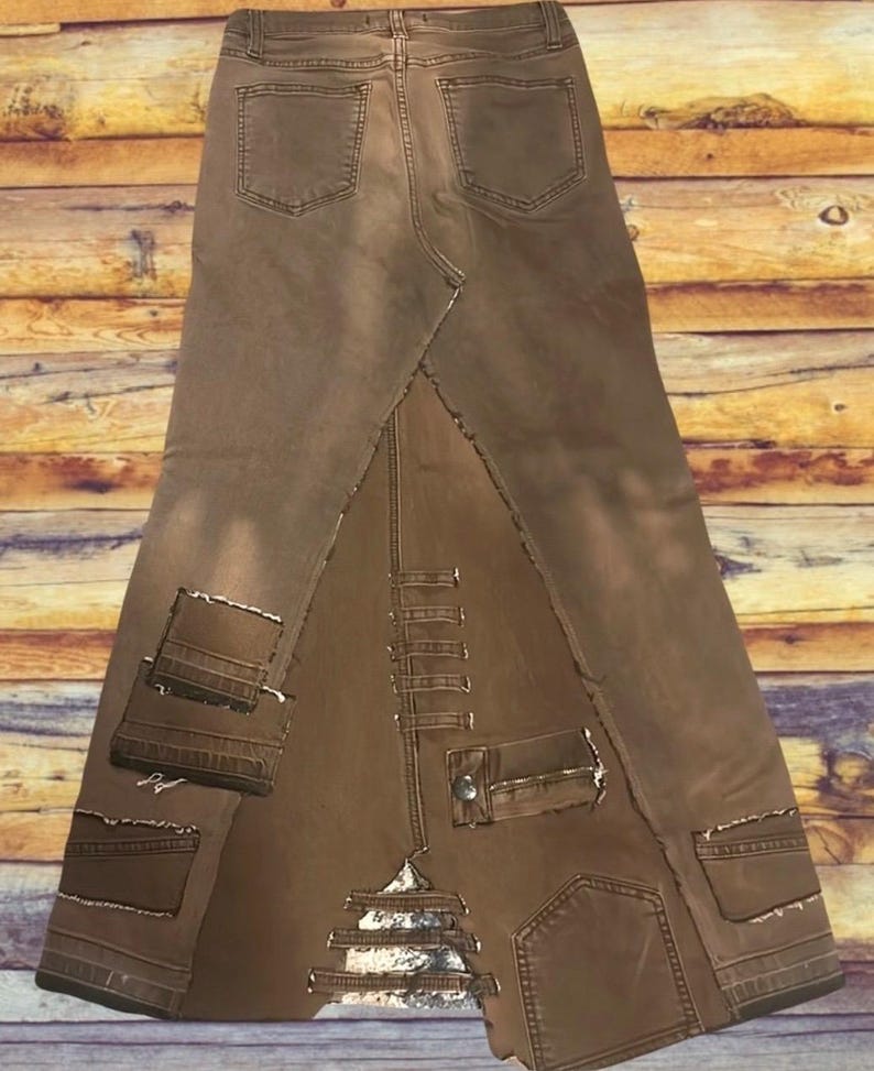 May include: A brown denim skirt with a unique design. The skirt features a patchwork construction with visible seams and pockets. The skirt has a high waist and a flared silhouette, with a distressed look. The skirt is made of denim.