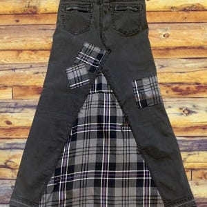 May include: A dark gray denim skirt with a plaid fabric panel and patches. The skirt features a classic five-pocket design, with plaid patches on the front and back. The plaid fabric is black, white, and gray.