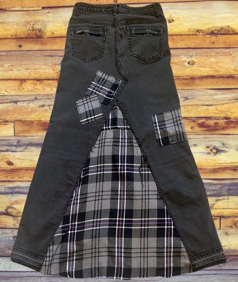 May include: A dark gray denim skirt with a plaid fabric panel and patches. The skirt features a classic five-pocket design, with plaid patches on the front and back. The plaid fabric is black, white, and gray.