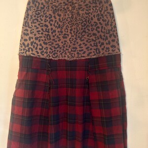 May include: A two-tone skirt with a unique design. The top portion features a brown leopard print, while the bottom half showcases a red and black plaid pattern. The skirt has a raw hemline, adding a touch of edginess to the garment.