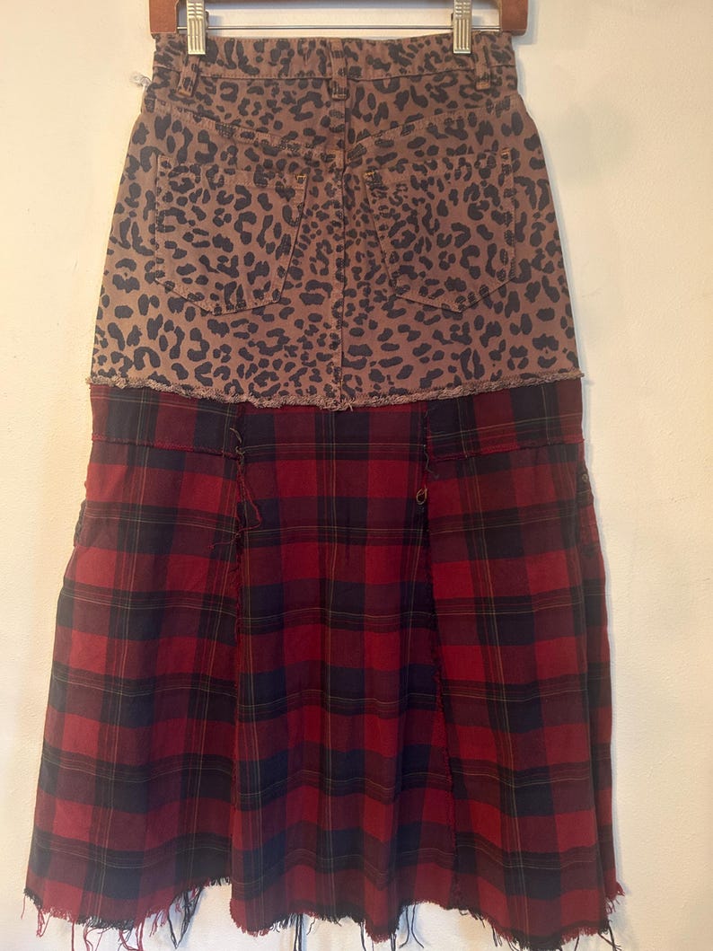 May include: A two-tone skirt with a unique design. The top portion features a brown leopard print, while the bottom half showcases a red and black plaid pattern. The skirt has a raw hemline, adding a touch of edginess to the garment.