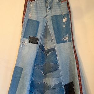 May include: Light wash denim skirt with patchwork and distressed details. Features a high waist, a split front, and a flared silhouette. Red and black plaid accents run down the sides. Patches and studs add visual interest to this unique skirt.