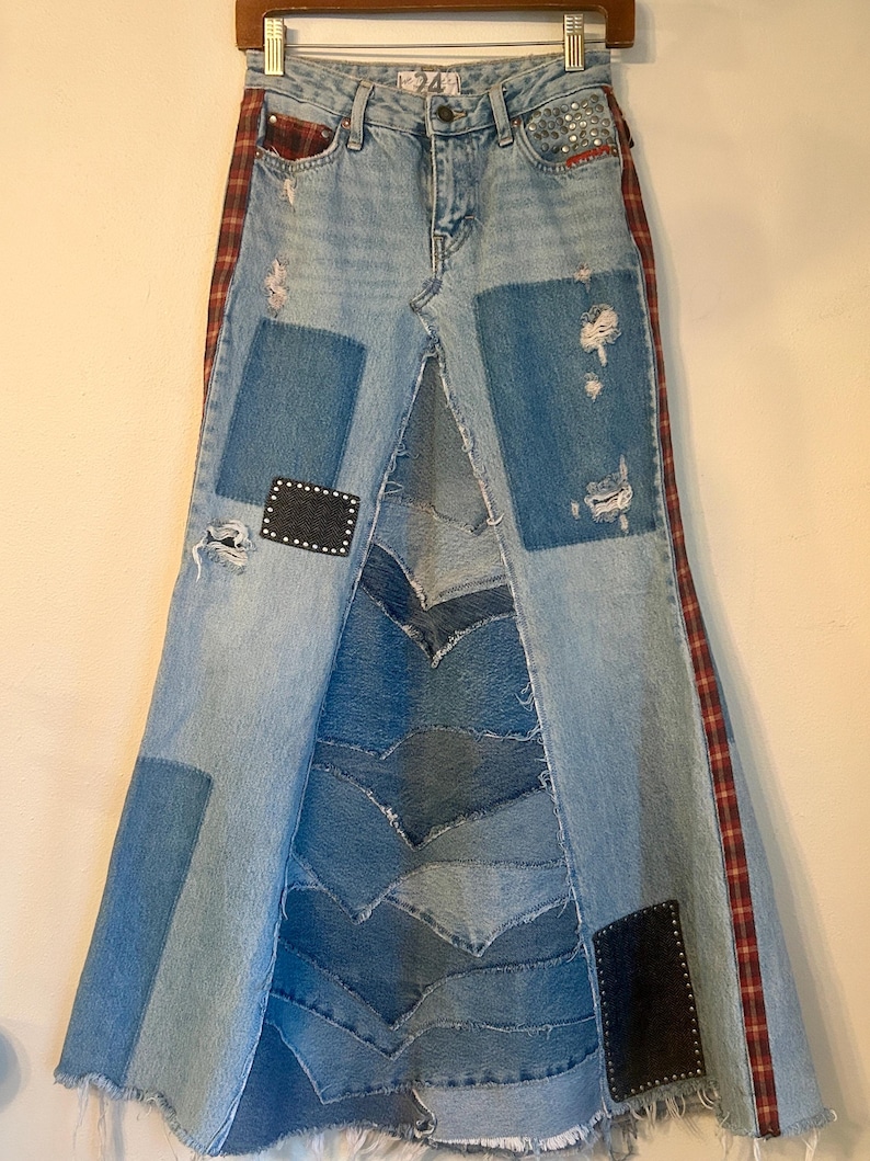 May include: Light wash denim skirt with patchwork and distressed details. Features a high waist, a split front, and a flared silhouette. Red and black plaid accents run down the sides. Patches and studs add visual interest to this unique skirt.