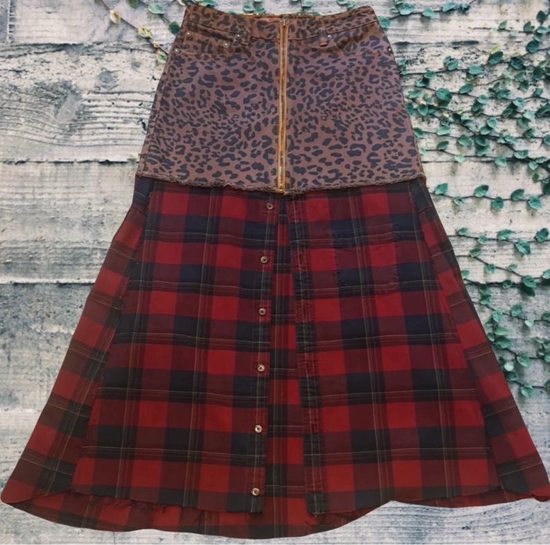 May include: A two-tone skirt featuring a leopard print denim top with a gold zipper and a red and black plaid bottom. The skirt has a button-down front and a unique, layered design.