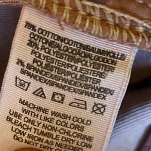 May include: Close-up of a fabric tag with text detailing the material composition: 78% cotton, 20% polyester, and 2% spandex. Washing instructions include machine wash cold with like colors, non-chlorine bleach, tumble dry low, and low iron.