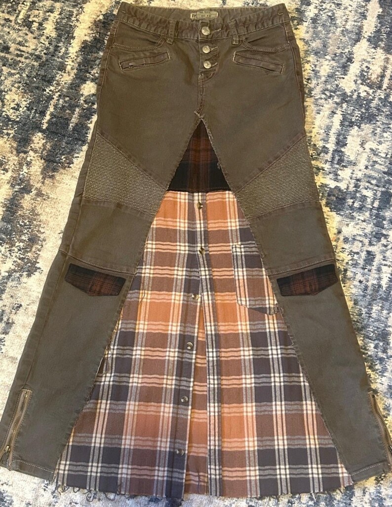 May include: A unique skirt design featuring a combination of materials. The top portion is a dark gray denim with button and zipper details. The skirt's lower section incorporates a plaid pattern in shades of brown, white, and gray.