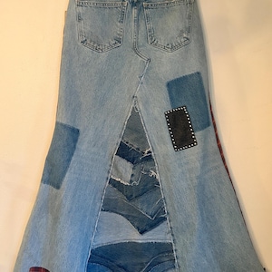 May include: A denim skirt with a patchwork design. The skirt features light blue denim with patches of darker denim and red plaid fabric. A black leather patch with silver studs is also visible.