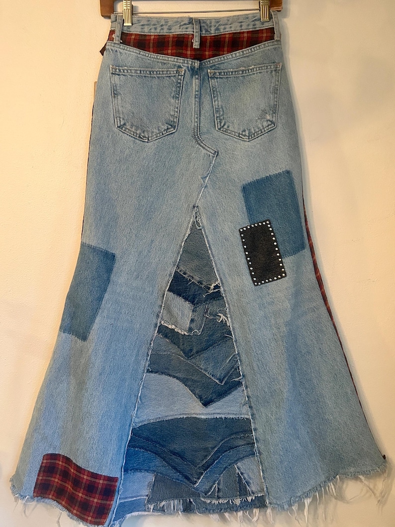May include: A denim skirt with a patchwork design. The skirt features light blue denim with patches of darker denim and red plaid fabric. A black leather patch with silver studs is also visible.