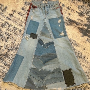 May include: A patchwork denim skirt with a flared silhouette. The skirt features various shades of blue denim patches, distressed details, and decorative accents. Patches of red plaid fabric are on the side.