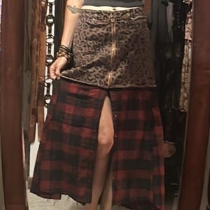 May include: A two-tone skirt with a leopard print top and a red and black plaid bottom. The skirt has a gold zipper and a button-down front. The skirt is knee-length and has a slit in the front.
