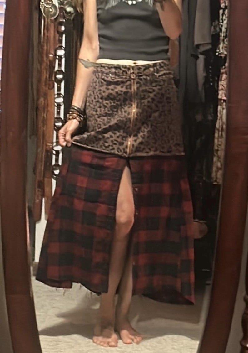 May include: A two-tone skirt with a leopard print top and a red and black plaid bottom. The skirt has a gold zipper and a button-down front. The skirt is knee-length and has a slit in the front.