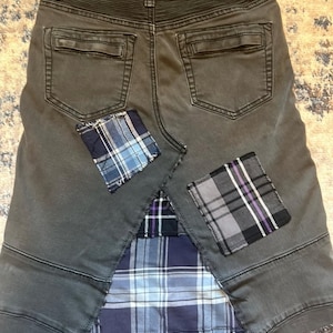 Puede incluir: Falda vaquera gris con parches de cuadros. La falda tiene dos bolsillos traseros y costuras decorativas. Parches de tela de cuadros azules, grises y morados est&aacute;n cosidos en la falda, agregando un dise&ntilde;o de patchwork &uacute;nico.