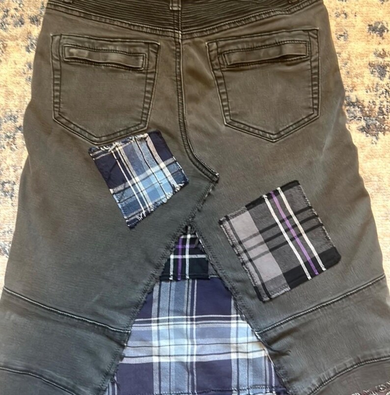 Puede incluir: Falda vaquera gris con parches de cuadros. La falda tiene dos bolsillos traseros y costuras decorativas. Parches de tela de cuadros azules, grises y morados est&aacute;n cosidos en la falda, agregando un dise&ntilde;o de patchwork &uacute;nico.
