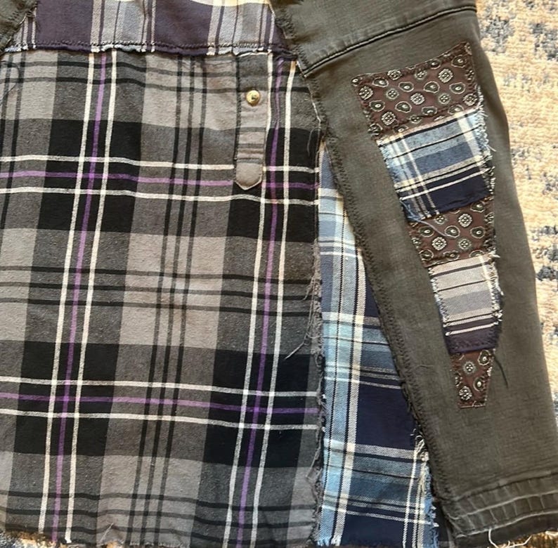 Puede incluir: Una camisa patchwork con un dise&ntilde;o de cuadros grises, negros y morados en la parte delantera. Las mangas son de mezclilla gris oscuro con parches decorativos de varios patrones azules y marrones. La camisa tiene cierre de botones.