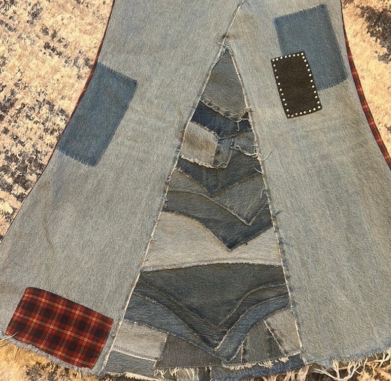 May include: A patchwork denim skirt with a unique design. The skirt features various shades of blue denim patches, with red and black plaid and a black patch with white dots. The skirt has a frayed hem.