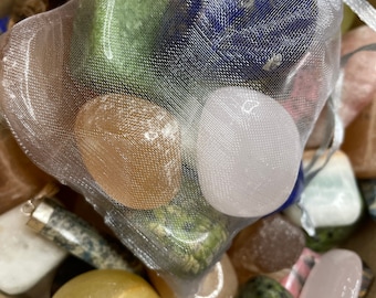 May include: A collection of tumbled stones in a white mesh bag. The stones are various colors, including green, blue, pink, and brown. The stones are in a bowl with other stones.