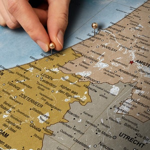 May include: A close-up of a map of the Netherlands with two gold push pins marking the locations of Leiden and Amsterdam. The map is printed on a brown background with white lines and black text.