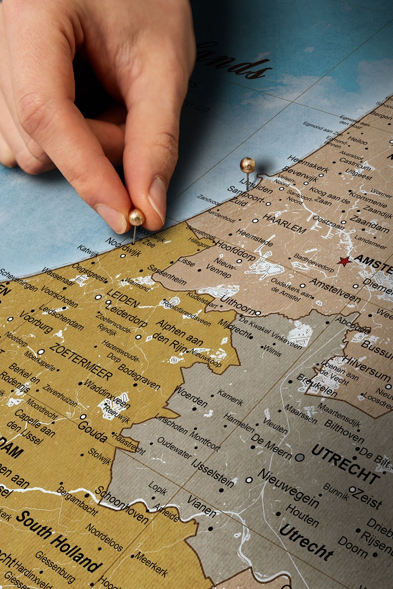 May include: A close-up of a map of the Netherlands with two gold push pins marking the locations of Leiden and Amsterdam. The map is printed on a brown background with white lines and black text.