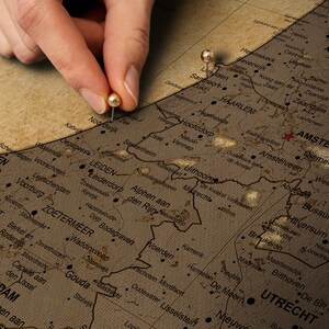 May include: A close-up of a vintage map of the Netherlands with push pins marking the cities of Leiden and Amsterdam. The map is on a brown background and has a worn, aged look.